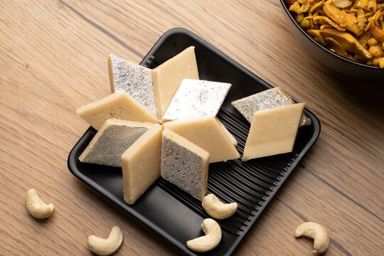 Diamond-shaped Kaju Katli slices arranged with almonds on a festive tray.